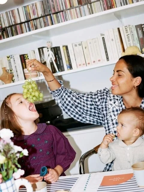 A grown-up lifting a bunch of grapes beside two children at a table.